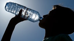 Profil eines Jungen, der aus einer Wasserflasche trinkt.