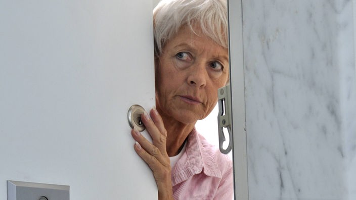 Eine ältere Frau schaut skeptisch aus der Haustür