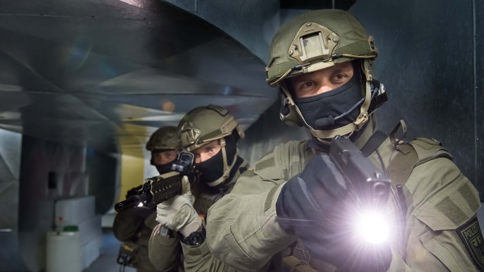 Drei bewaffnete GSG9-Anwärter stehen bewaffnet hintereinander. | Bildquelle: Bundespolizei Drei bewaffnete GSG9-Anwärter stehen bewaffnet hintereinander.