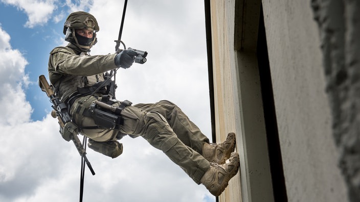 GSG-9-Anwärter seilt sich an einer Hauswand ab mit einer Waffe in der Hand. | Bildquelle: Bundespolizei GSG-9-Anwärter seilt sich an einer Hauswand ab mit einer Waffe in der Hand.