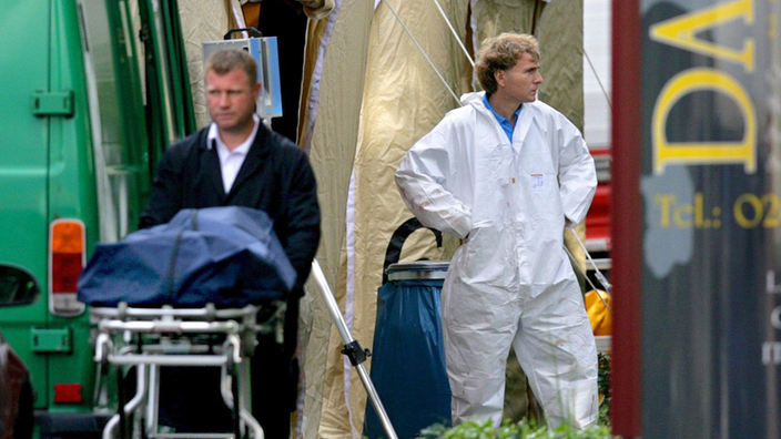 Eine Leiche in einem Leichensack wird von einem Bestatter in Duisburg vom Tatort zu einem Leichenwagen geschoben.