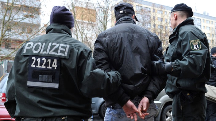 Polizisten führen einen mit Handschellen gefesselten Mann zu einem Pkw. Der Mann gehört zu den acht Menschen, die nach Angaben der Polizei bei einem Großeinsatz gegen Drogendealer auf dem U-Bahnhof Heinrich-Heine-Straße in Berlin festgenommen wurden