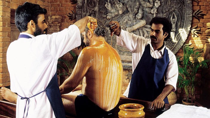 Zwei indische Ayurveda-Ärzte übergießen den Rücken eines Mannes mit Öl