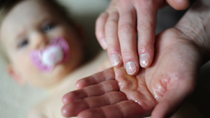 Eine Mutter verreibt das Massageöl in den Händen.