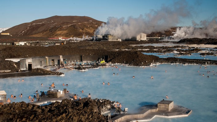 Steinige Landschaft auf Island mit heißen, blauen Wasserflächen über denen Dampf aufsteigt.