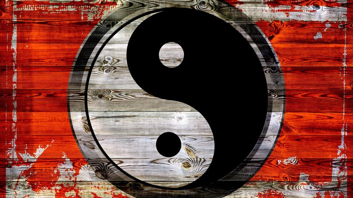 Das schwarz-weiße Yin-Yang-Symbol aufgemalt auf einem roten Holzhintergrund