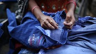 Eine Frau näht an einer Jeans in dem Slum Shastri Park in Delhi, Indien