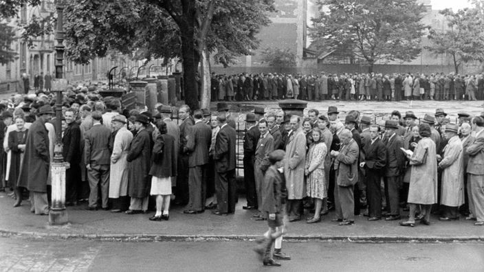 Menschen in den 40er Jahren bilden auf einem Platz eine riesige Warteschlange.