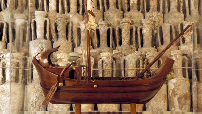 Das Modell eines römischen Schiffs steht vor römischen Amphoren 