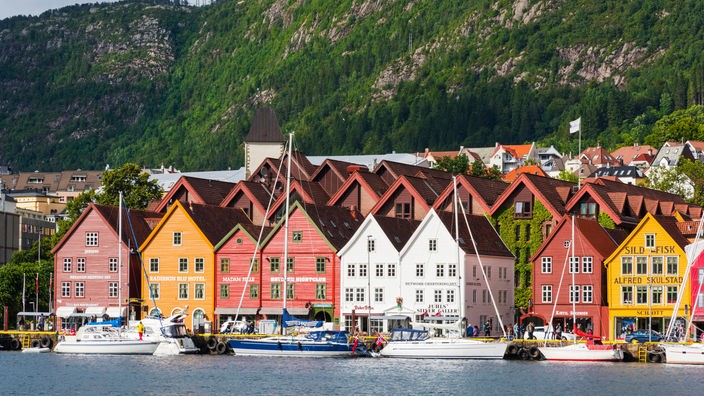 Vor einer Bergkulisse stehen kleine Häuser im Hafen von Bergen, Norwegen