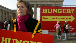 Eine Frau hält vorm Brandenburger Tor ein Protestplakat hoch. Auf dem Plakat steht das Wort Hunger.