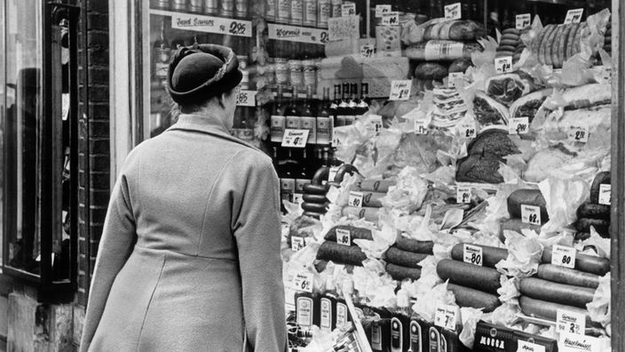 Eine Frau vor dem gefüllten Schaufenster eines Feinkostgeschäfts, um 1949