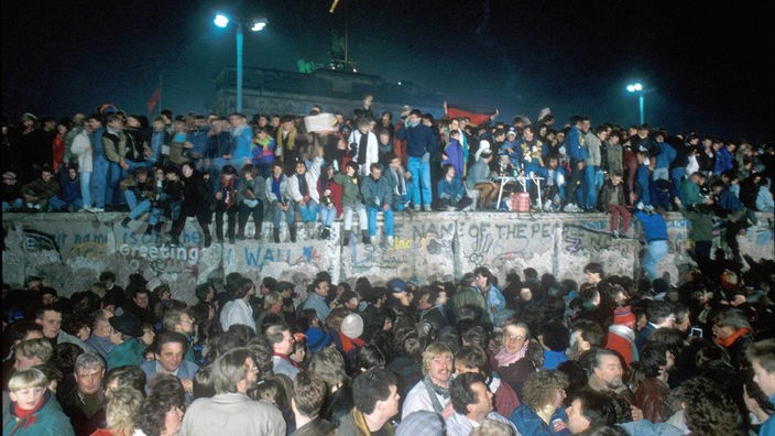 Herbst 1989, vor dem Brandenburger Tor steht eine Menschenmenge auf der Berliner Mauer