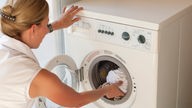 Eine Frau legt Wäsche in die Trommel einer Waschmaschine