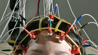 Eine Frau mit zahlreichen Kabeln am Kopf.