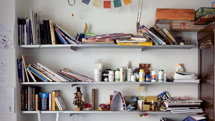 Blick auf einen vollgestopften Schreibtisch und Regale mit Tabletten, Büchern und Kleinkram.