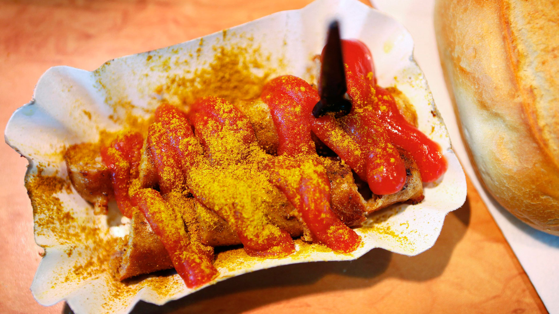 Currywurst auf dem Pappteller neben einem Brötchen.