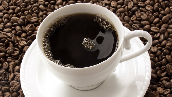 Eine Tasse Kaffee steht auf Kaffeebohnen.