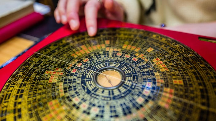 Eine Hand bewegt einen durchsichtigen chinesischen Kompass