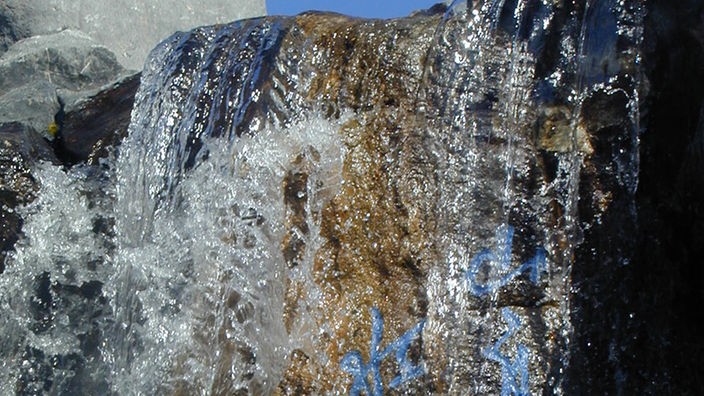 Künstlicher Wasserfall. Auf den Steinen, über die das Wasser fließt, steht ein Gedicht in blauen chinesischen Schriftzeichen.