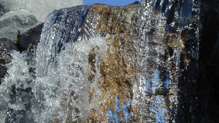Künstlicher Wasserfall. Auf den Steinen, über die das Wasser fließt, steht ein Gedicht in blauen chinesischen Schriftzeichen. | Bildquelle: Grün Berlin Künstlicher Wasserfall. Auf den Steinen, über die das Wasser fließt, steht ein Gedicht in blauen chinesischen Schriftzeichen.