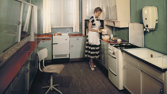 Eine Hausfrau steht in ihrer Einbauküche und rührt in einer Schüssel.