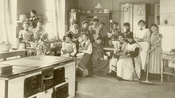 Schwarzweiß-Foto einer Gruppe von Frauen, die neben einem großen Herd sitzen und stehen | Bildquelle: AKG Schwarzweiß-Foto einer Gruppe von Frauen, die neben einem großen Herd sitzen und stehen