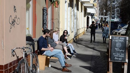 Studenten und Künstler sitzen vor einem Kaffe- und Plattenladen in Berlin-Neukölln