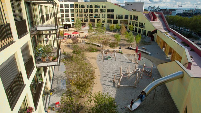 Gebäude-Innenhof mit Bäumen, Spielgeräten, teilweise Sand, teilweise gepflastert
