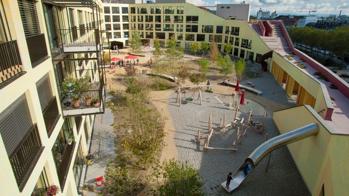 Gebäude-Innenhof mit Bäumen, Spielgeräten, teilweise Sand, teilweise gepflastert | Bildquelle: Genossenschaft Kalkbreite, Volker Schopp Gebäude-Innenhof mit Bäumen, Spielgeräten, teilweise Sand, teilweise gepflastert