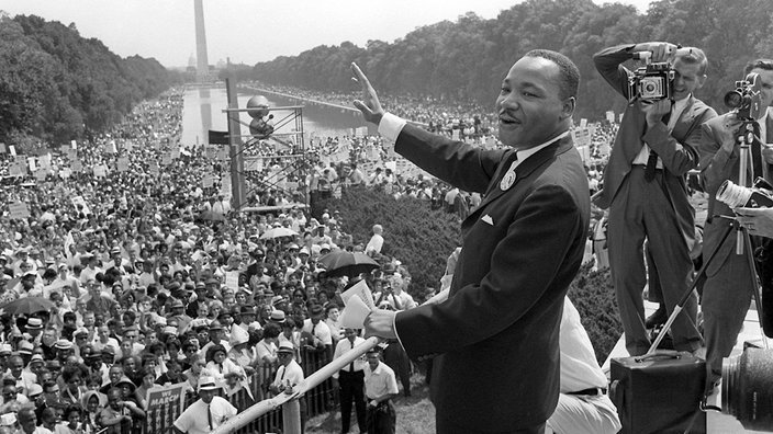 1963: Der US-Bürgerrechtler Martin Luther King winkt bei einer Kundgebung von der Lincoln-Gedächtnisstätte in Washington aus seinen Anhängern zu. | Bildquelle: picture alliance/dpa 1963: Der US-Bürgerrechtler Martin Luther King winkt bei einer Kundgebung von der Lincoln-Gedächtnisstätte in Washington aus seinen Anhängern zu.