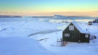 Aufnahme einer Eislandschaft mit Holzhütte in Westgrönland zur Abendzeit.