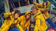 Zeichnung: Vier Kinder in strahlend gelben Wachsjacken, in ihrer Mitte der Hund Timmy. Sie sind an Bord eines Schiffes.