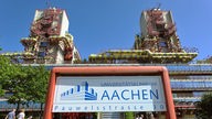 Schild mit der Aufschrift "Universitätsklinikum Aachen" und dem High-Tech-Gebäude im Hintergrund.
