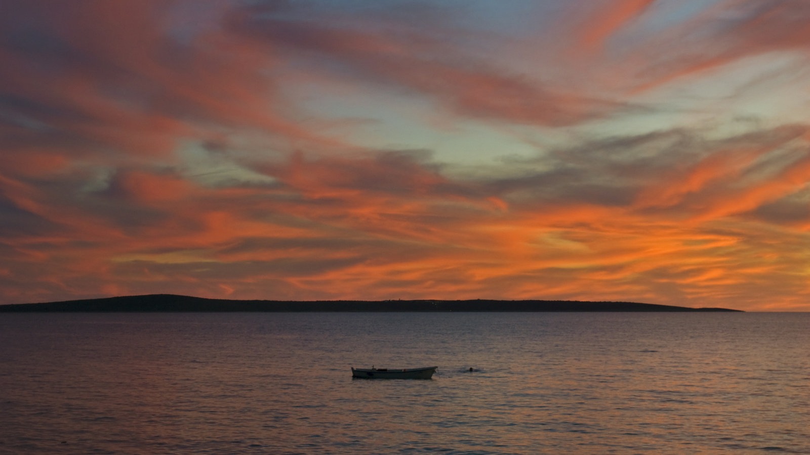 Von der untergehenden Sonne rot beleuchtete Wolken über einer Insel.