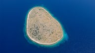 Luftbild einer fast runden, kargen Insel im tiefblauen Meer.