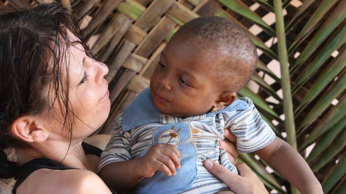 Eine weiße Frau hält ein afrikanisches Kind