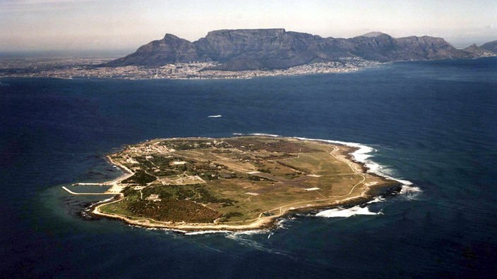 Luftbild: Im Vordergrund die Insel Roben Island. Im Hintergrund die Küste Kapstadts mit dem Tafelberg.