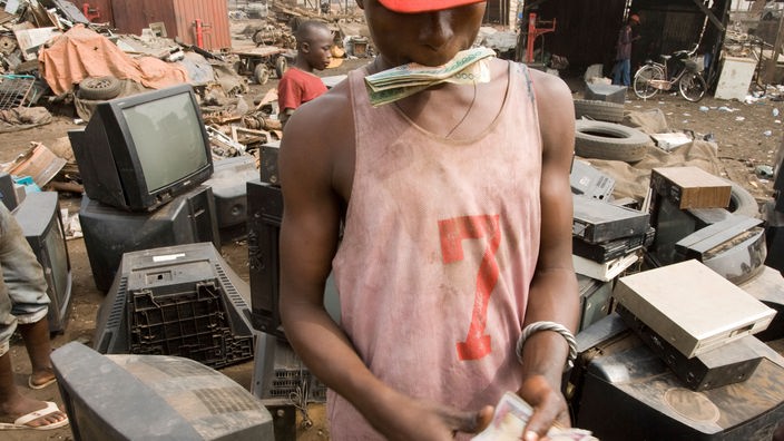 Junge auf der Giftmüllhalde Agbogbloshie mit einem Bündel Geldscheinen in der Hand.