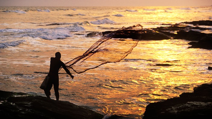 Ein Fischer wirft bei Sonnenaufgang seine Netze ins Meer.