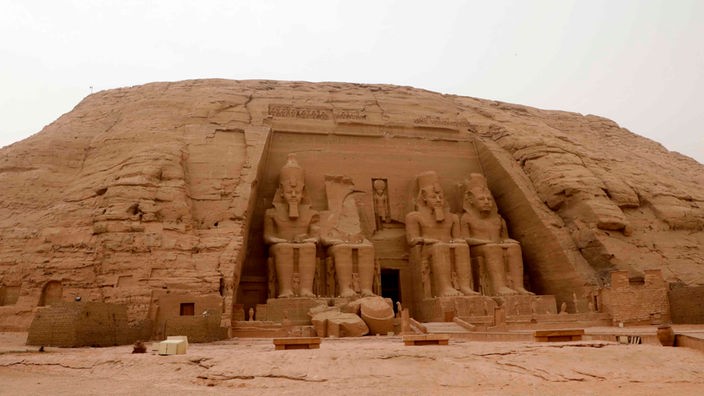 Der Eingang einer Tempelanlage wird von riesigen, sitzenden Skulpturen gesäumt, die zweite von links ist zerstört