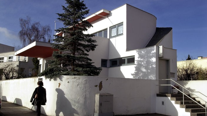 Weißes Wohngebäude der Weißenhof-Siedlung mit großzügiger Terrasse, rund geschwungener Mauer und flachem Dach.