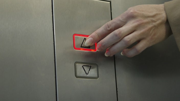 Eine Frauenhand drückt die Aufwärtstaste an einem Fahrstuhl. 