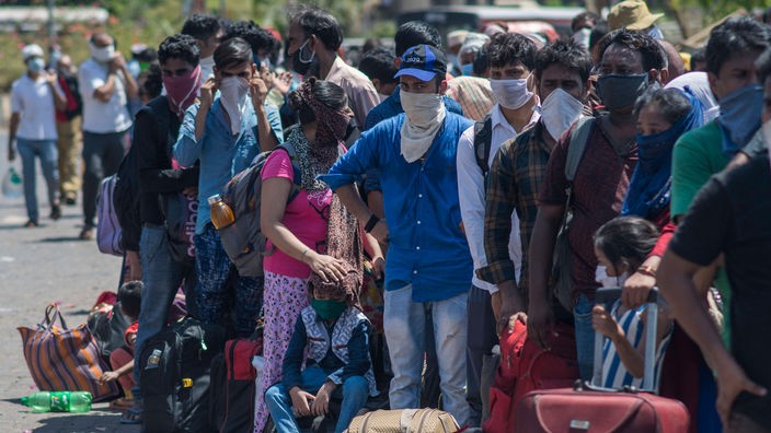 Indische Wanderarbeiter mit Masken stehen in einer Reihe.