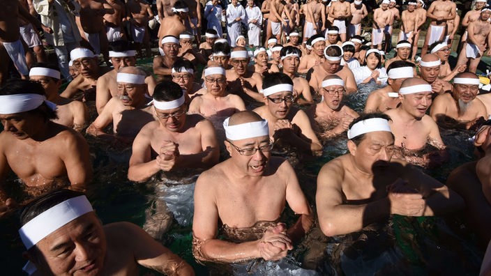 Zahlreiche Männer hocken in einem Pool mit eiskaltem Wasser, das ihnen bis zur Brust geht. Sie sind ins Gebet vertieft. Um den Kopf tragen sie ein weißes Stirnband.