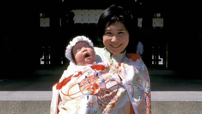 Eine japanische Mutter mit ihrem Baby vor einem Schrein