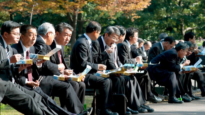 Japanische Manager mit Lunchpaketen im Park | Bildquelle: picture-alliance/ dpa/dpaweb Japanische Manager mit Lunchpaketen im Park