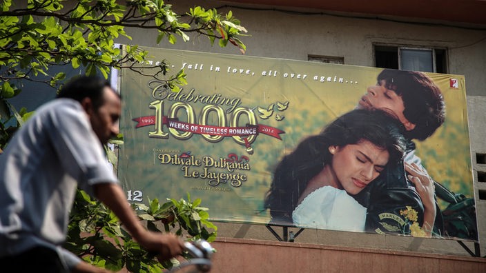 Ein Fahrradfahrer fährt an einem großen Plakat eines Bollywood-Films vorbei.