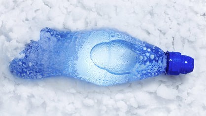 Eine Plastikflasche mit flüssigem Wasser liegt im Schnee.