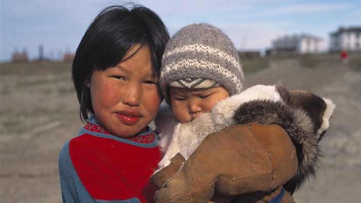 Ein größeres Kind vom Stamm der Tschuktschen hält einen Säugling, der dick eingepackt ist, im Arm.